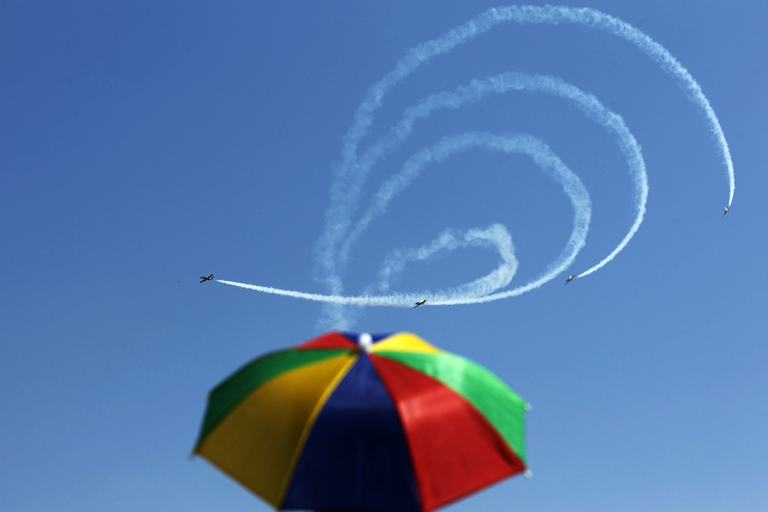 July 27, 2013. A man wearing a sun-protective umbrella watches Latvia's Baltic Bees aerobatic team performing on L-39C Albatross airplanes during Bucharest International Air Show at Baneasa airport.