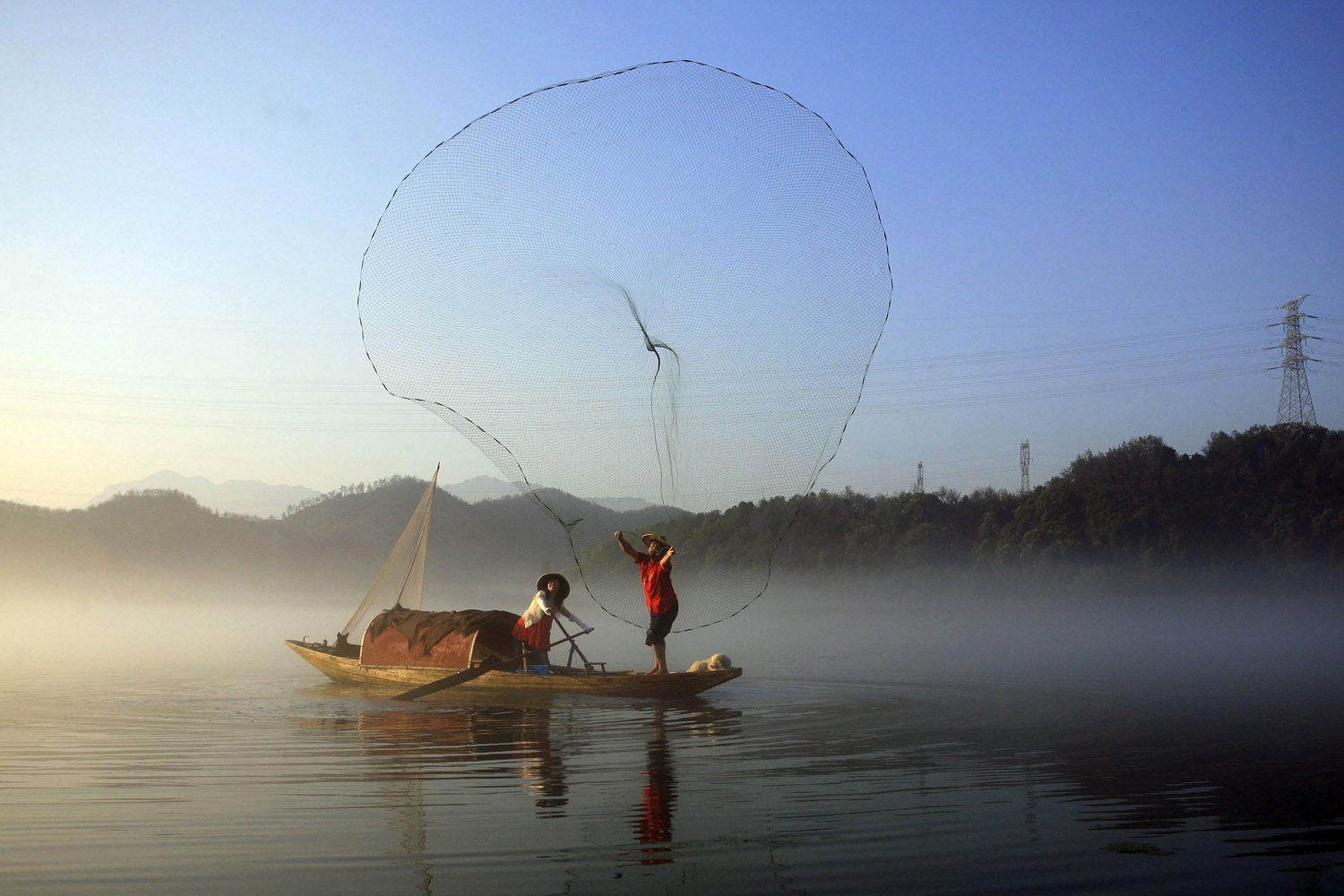 A fisherman casts his net to catch fish on Xin'an River in Jiande