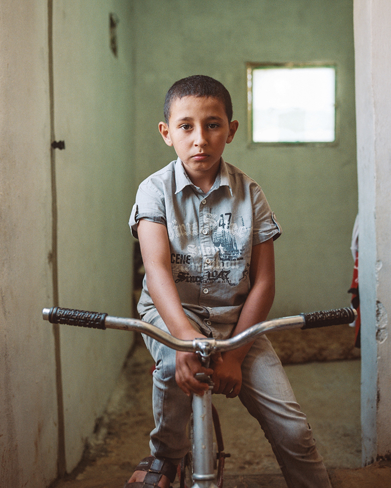Aghyad Ghassan Al-Jughmani, 10, sits on his bike in the small home his family currently stays in for free on the outskirts of Amman, Jordan.