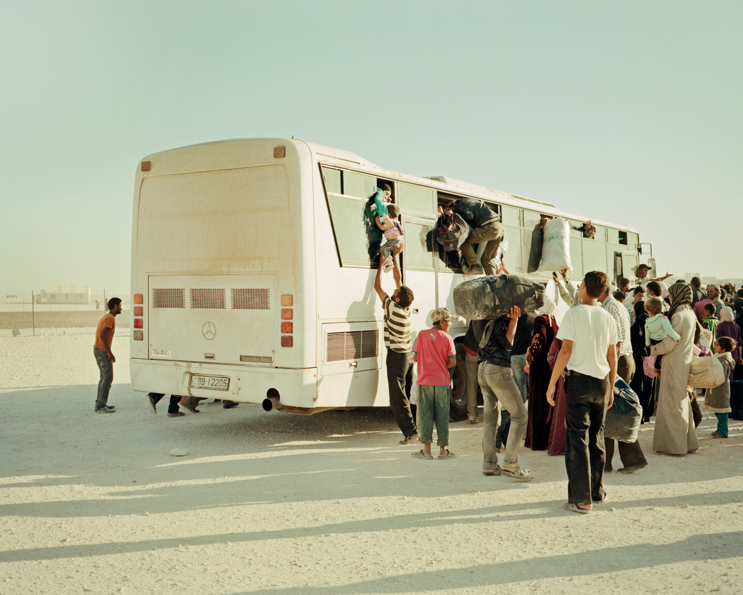 A Syrian man pushes a young boy through the window of a bus while other climb in and push luggage on. The bus is one of three that leave the Zaatari refugee camp every day to return to Syria. The buses, paid for by the Jordanian government, take refugees across the border where they are either met by a Free Syrian Army escort or left to find their own way to their towns and villages. In July, an average of 300 people a day were leaving the camp to return to Syria.