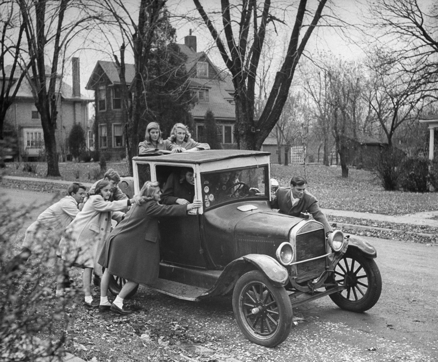 Gang of teen-agers push boyfriend's model T to get it started. Car is 17 years old and can hold 12 boys and girls. Favorite ride is out to football game.