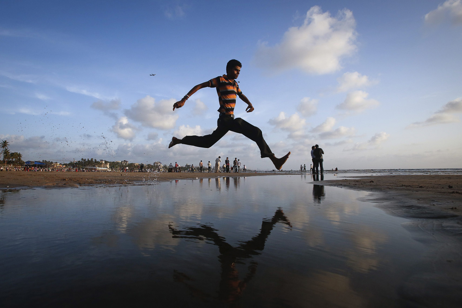 A man jumps over a water stream on a beach along the Arabian Sea in Mumbai