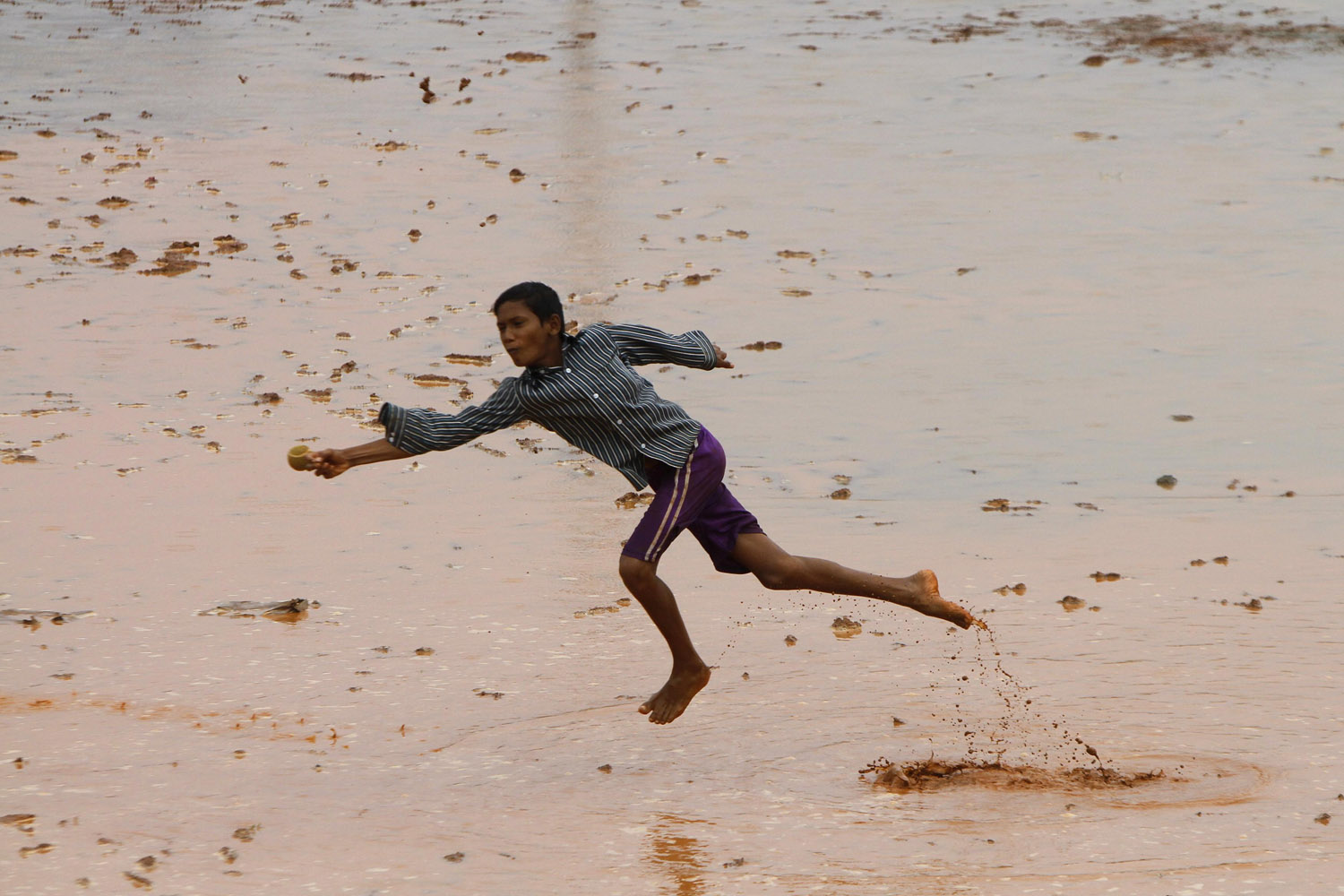 A boy dives to catch the ball while playing cricket in a water-logged play ground in Chennai