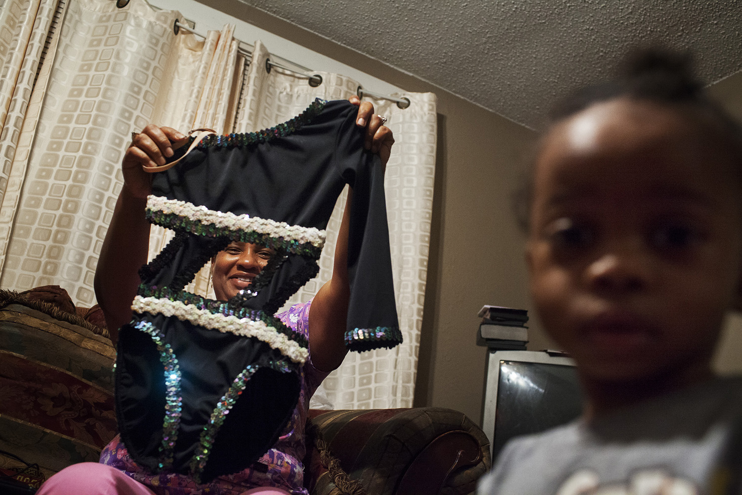 Kentrell's mother holds up a leotard he designed and customized, admiring his craftsmansip. Kentrell designs many of the costumes for the Prancing Elites, often working on a shoestring budget to create eye-catching and exciting matching outfits for performances. The Prancing Elites are a group of young, gay, black men who practice J-Sette, a form of dance birthed at Historically Black Colleges that is characterized by sharp, cheerleading-style movements and hip-hop performed to an eight-count beat. Traditionally, men cannot join college dance teams, so young gay black men have been forming their own J-Sette "lines," organizing competitions, and creating their own outlets to practice this type of dance.