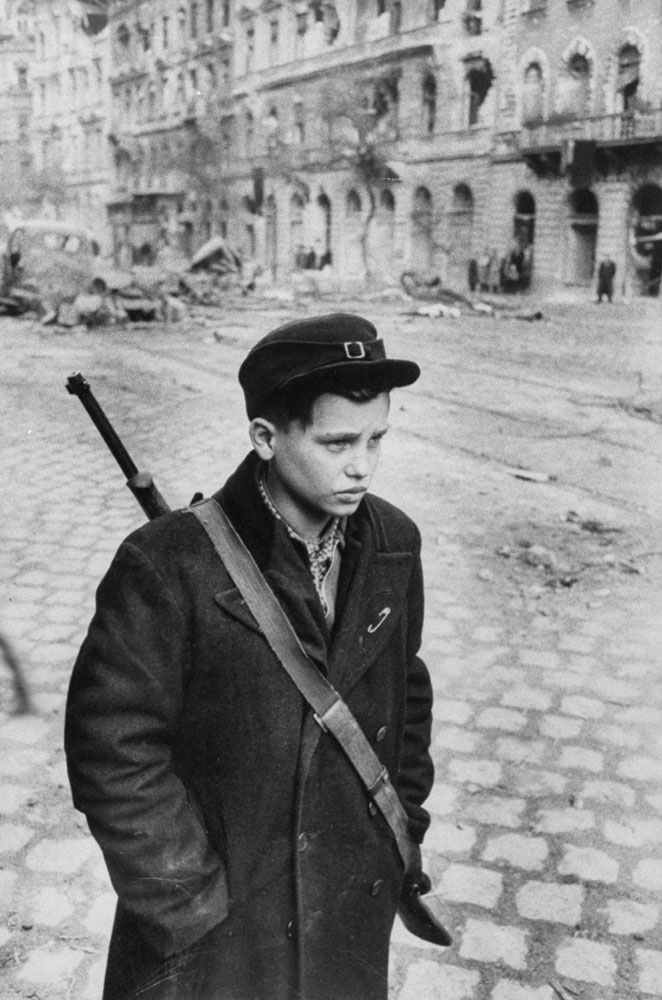Caption from LIFE.  On a man's mission, Pal Pruck, 15, was one of the many brave teen-agers who fought in the rebellion. He is standing in a rubble-strewn Budapest street.