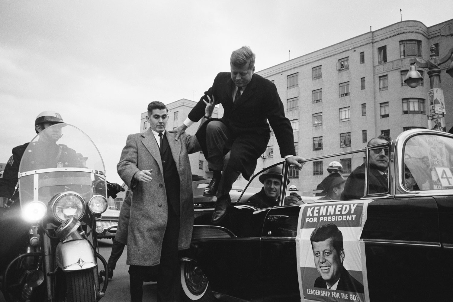 Presidential candidate John F. Kennedy leaps from a car while campaigning, 1960.