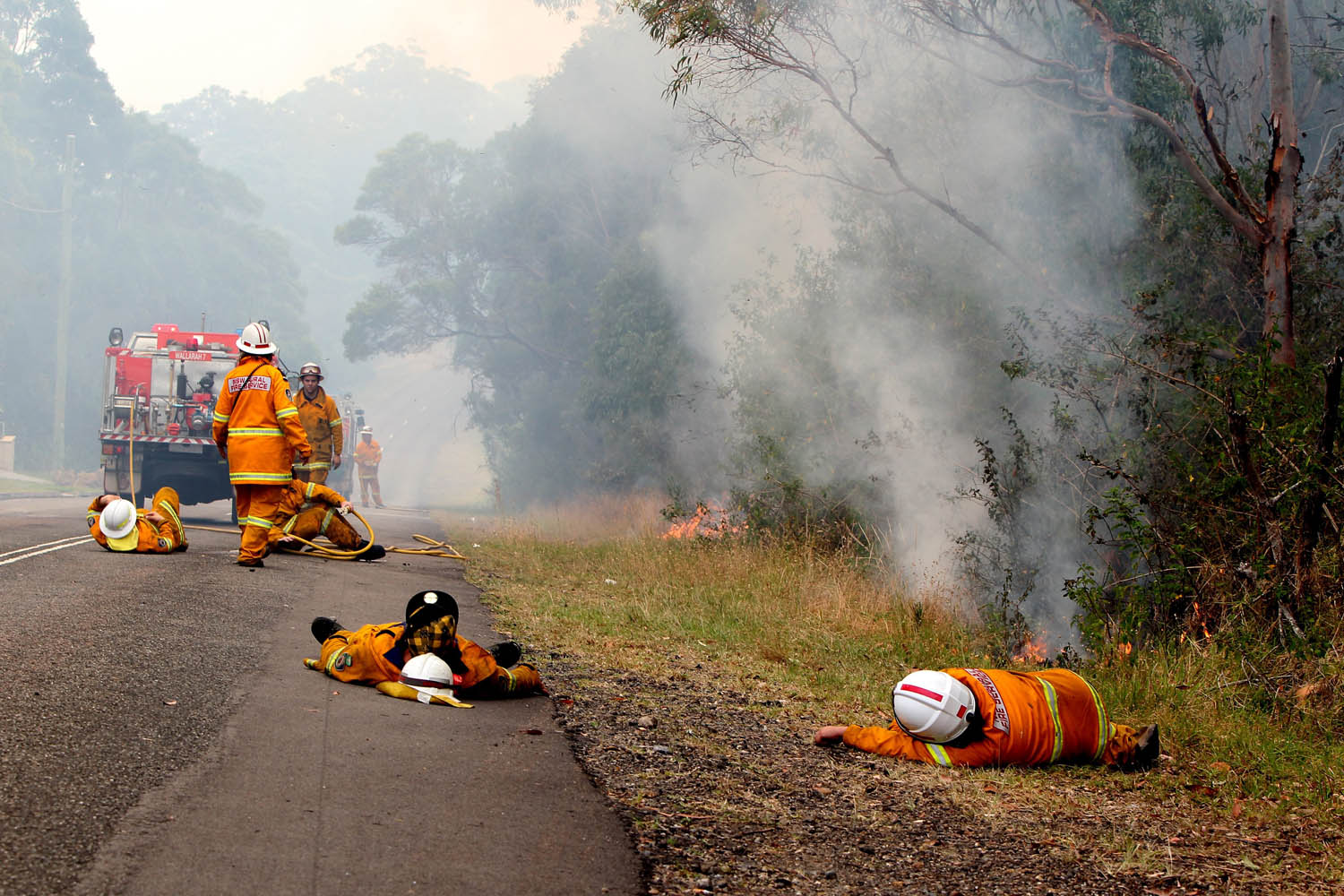 Oct. 18, 2013. Exhausted firefighters take a rest while fire burns close by, on Crangan Bay Road in Nords Wharf, Australia.