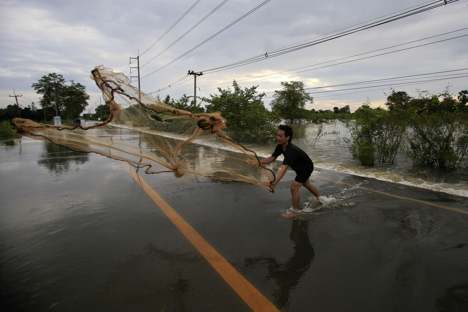 A man casts a fishing net on a flooded street at Srimahaphot district in Prachin Buri