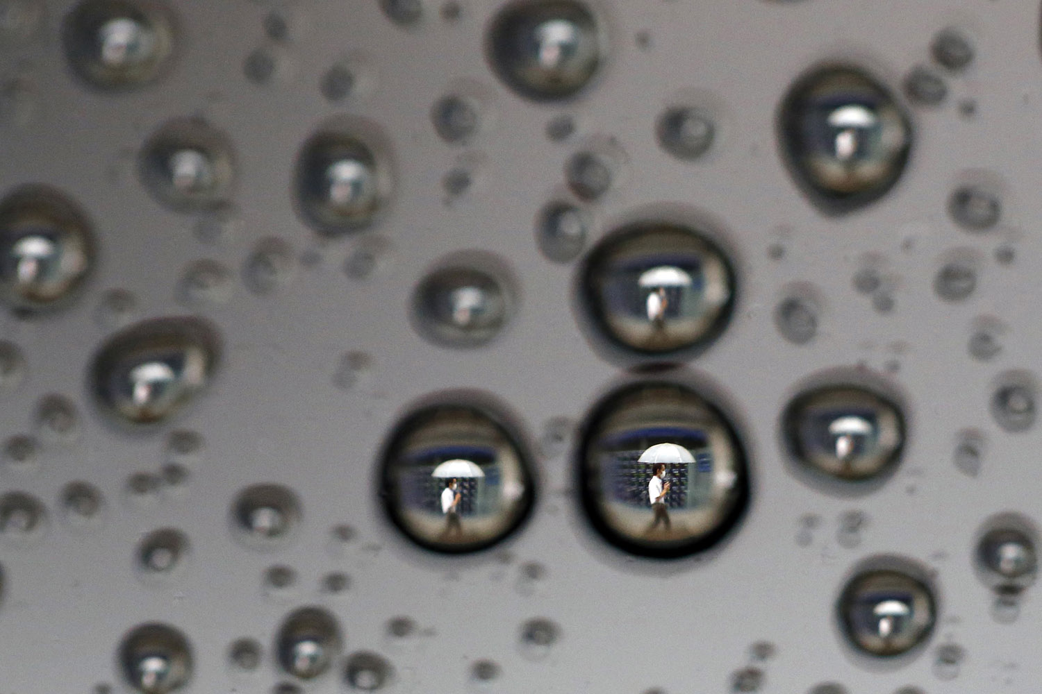 Oct. 2, 2013. Rain drops on a car window reflecting a man walking past a stock index board in Tokyo.