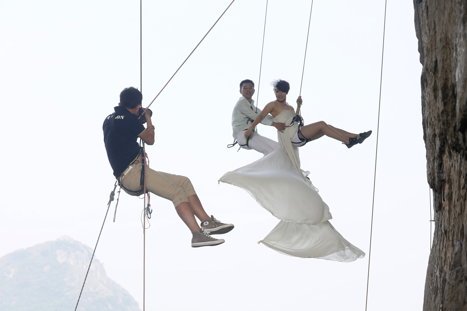A photographer takes pictures of Fang in a wedding gown next to her husband as they hang from a cliff during a rock climbing exercise in Liuzhou