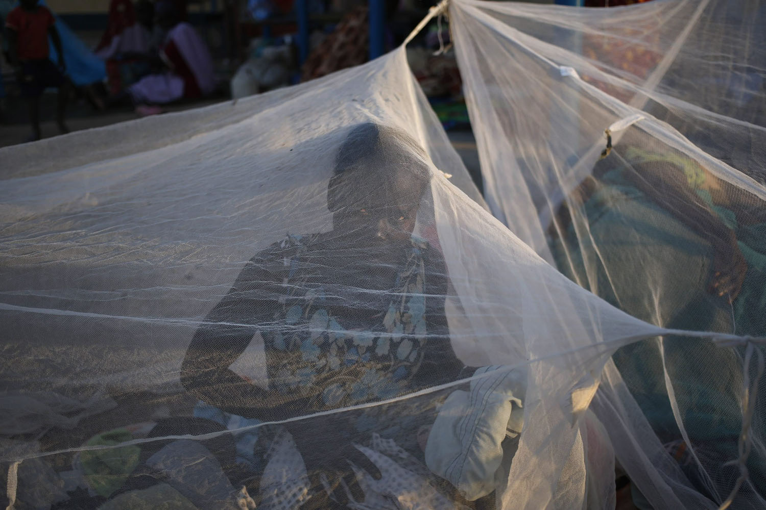 A woman sits inside a mosquito tent near a polling station located in a school during a referendum in the town of Abyei