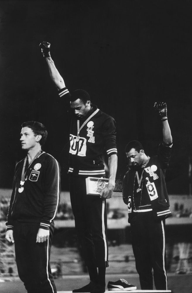 Tommie Smith (center) and John Carlos (right) raise black-gloved fists during the American national anthem; Australian silver medalist Peter Norman, who supported their protest, is at left.