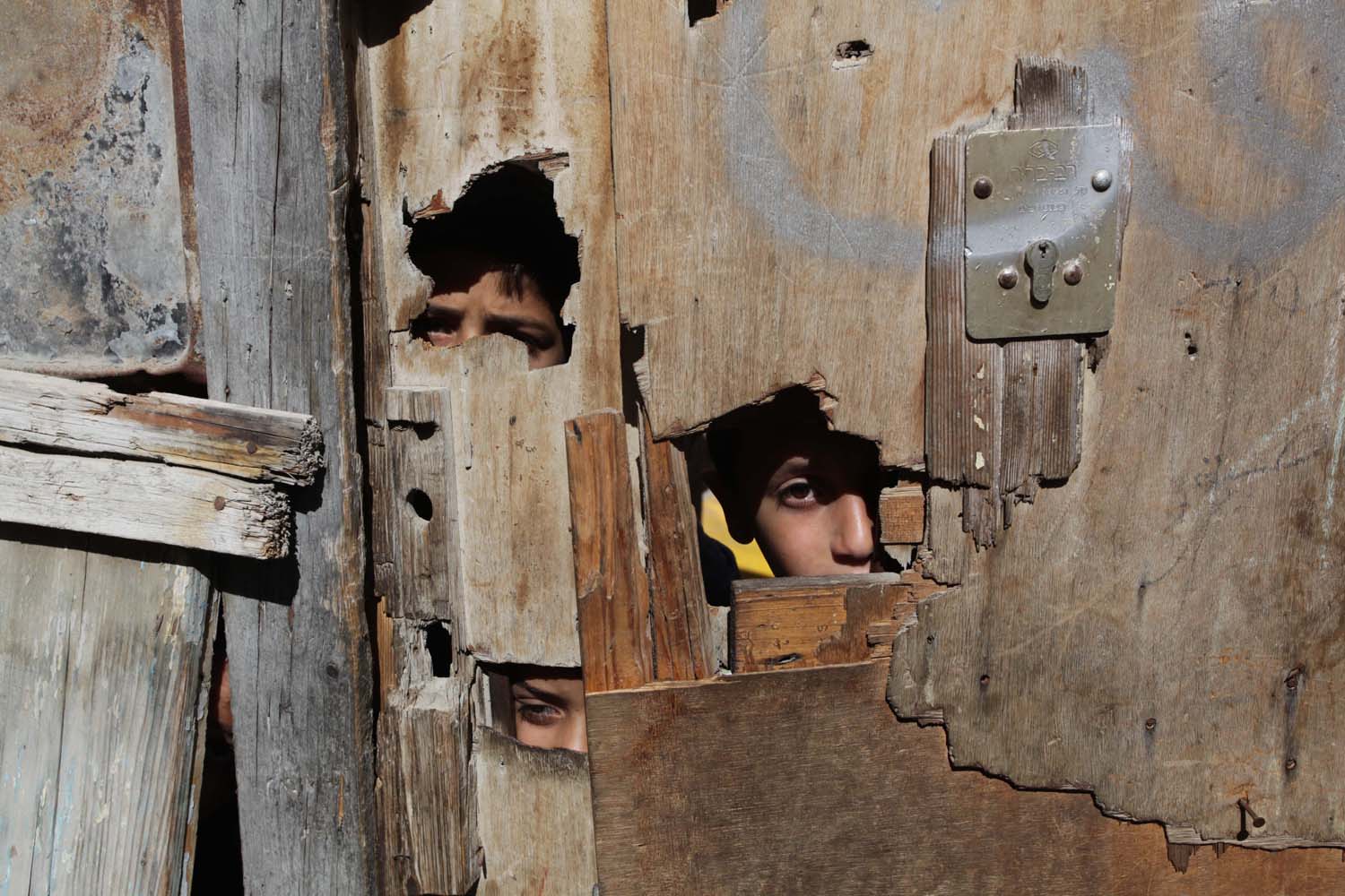 PALESTINIAN GIRLS LOOK THROUGH A WOODEN DOOR AT AL-SHATI REFUGEE CAMP