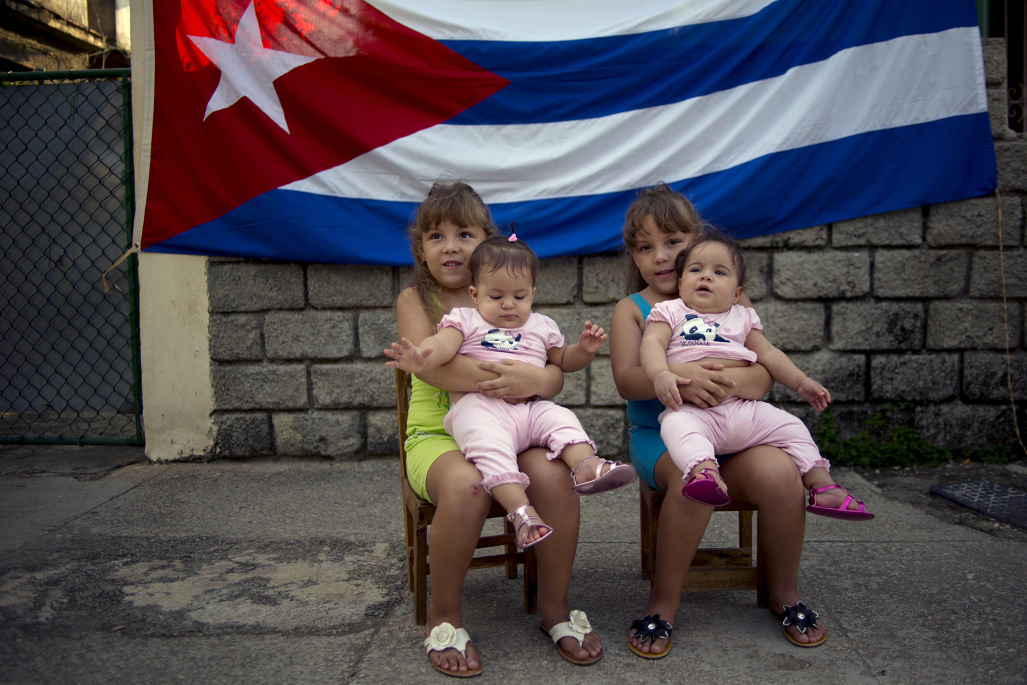 Sept. 29, 2013 Six-year-old twins Asley and Aslen Velazquez hold eight-month-old twins Tiffani and Stessany Valles as they pose for portraits in front a Cuban flag on their street in Havana, Cuba.