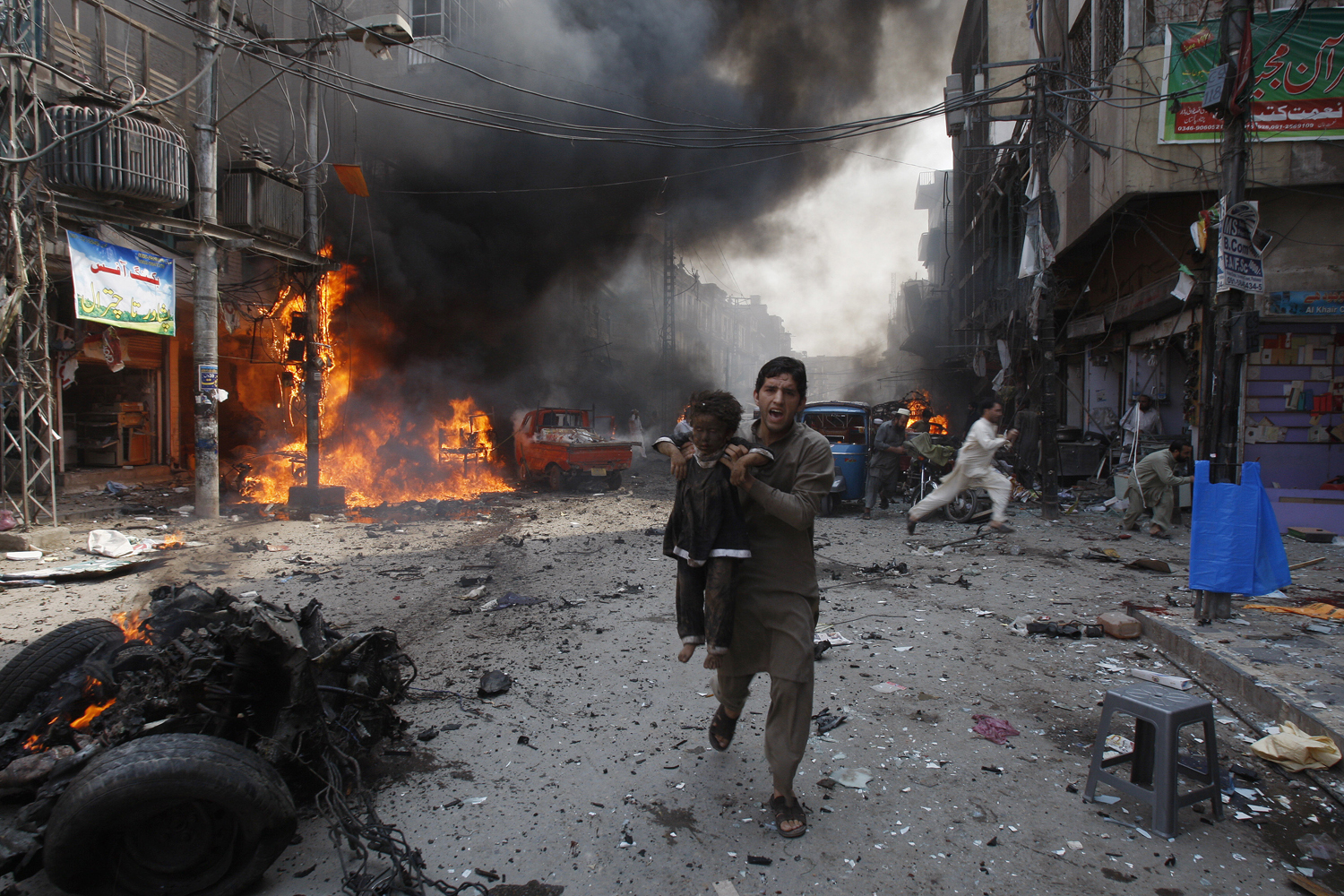 Sept. 29, 2013. A Pakistani man carrying a child rushes away from the site of a blast shortly after a car exploded in Peshawar, Pakistan.