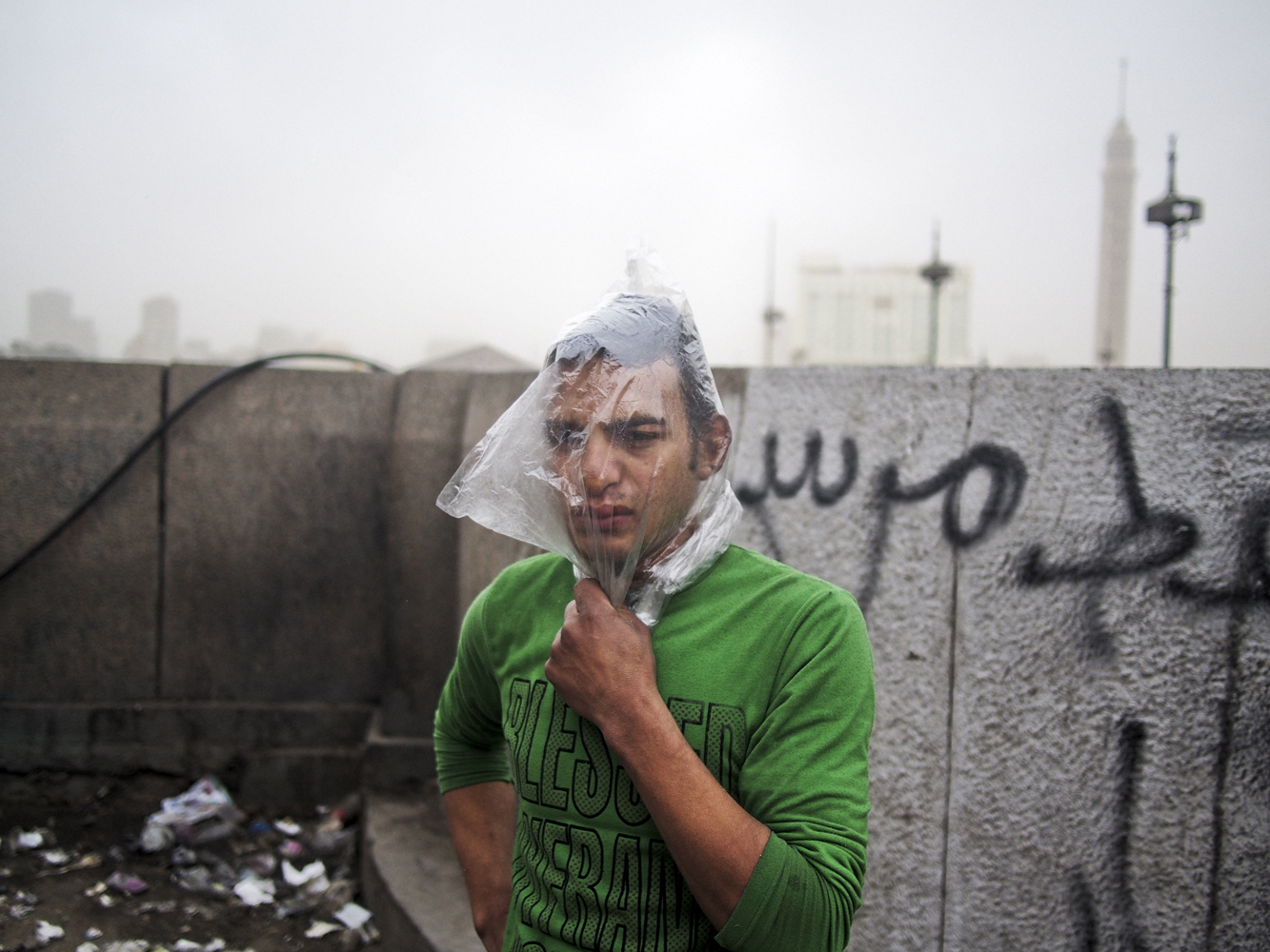 EGYPT. Cairo. January 28, 2013. A protestors covers his head with a plastic bag as a makeshift gas mask during clashes near Tahrir Square.