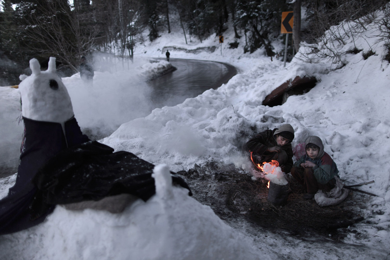 Jan. 9, 2013. Pakistani Anwar Ali, 13, center, and his brother Hamad, 8, sit around a fire to warm themselves from the cold, while waiting for customers to pose for a picture next to a snow statue they built on a roadside, in Murree, near Islamabad.