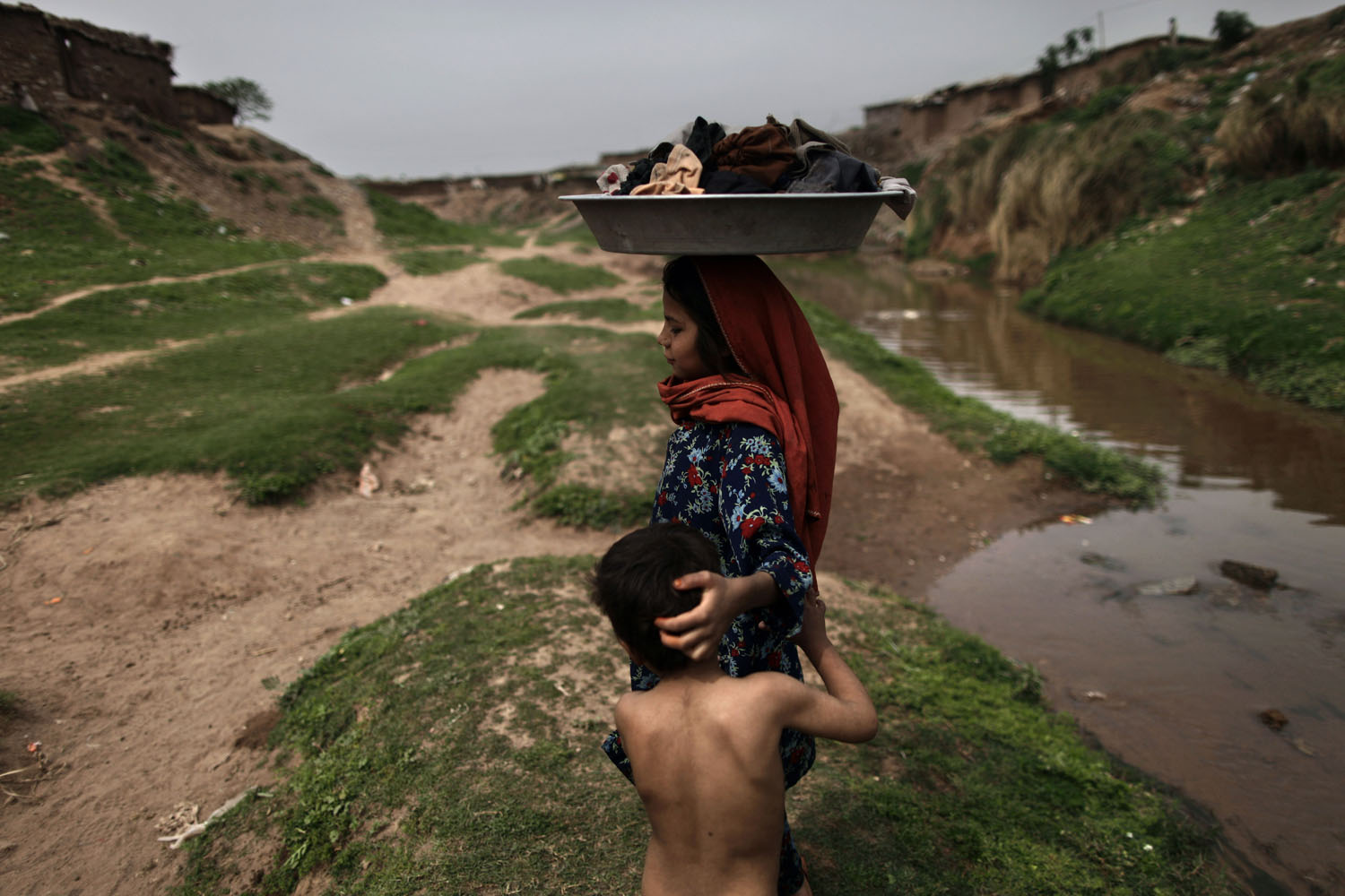 March 22, 2013. An Afghan refugee girl carries her laundry on her head after washing it in a polluted stream on World Water Day in a poor neighborhood on the outskirts of Islamabad. The U.N. estimates that more than one in six people worldwide do not have access to 20-50 liters (5-13 gallons) of safe freshwater a day to ensure their basic needs for drinking, cooking and cleaning.