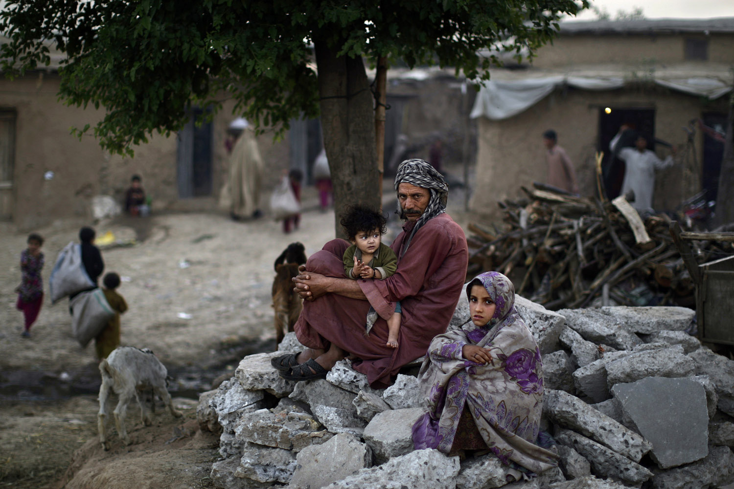 April 11, 2013. Pakistani daily laborer Wakeel Mohammed, 38, sits on a roadside with his daughter Halimah, 1, on his lap and his relative Khadijah, 7, right, near their home, in a poor neighborhood on the outskirts of Islamabad. Wakeel and his family fled Pakistan's tribal region of Mohmand Agency, due to fighting between the Taliban and the army, and took refuge in Islamabad.