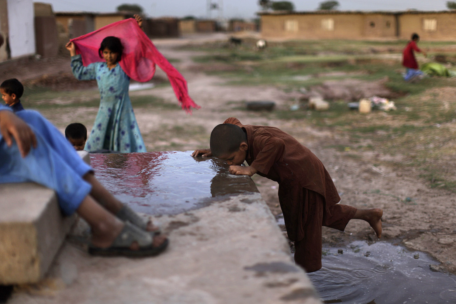 May 15, 2013. An Afghan refugee, right, drinks water leaked from a water point on the outskirts of Islamabad.