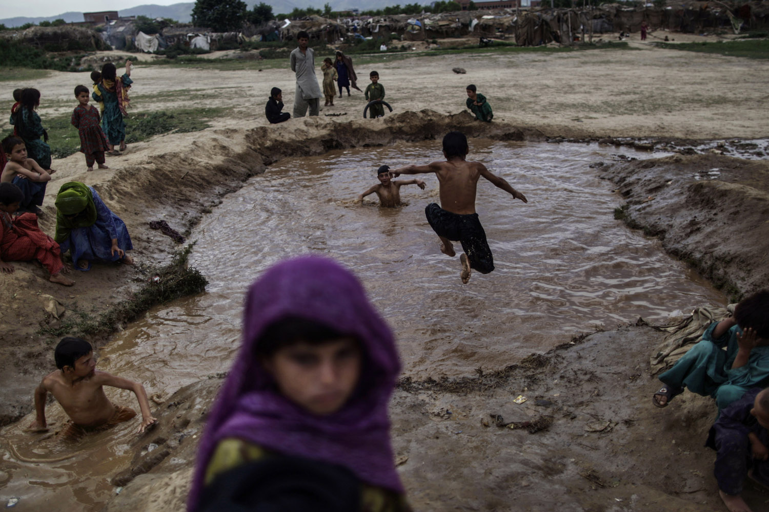 June 17, 2013. Afghan refugee children swim in muddy water created from a broken water pipe on the outskirts of Islamabad.