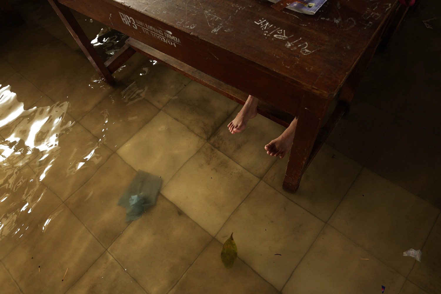 The bare feet of a student are pictured below a table in a flooded classroom in Lopang Domba Elementary School in Serang