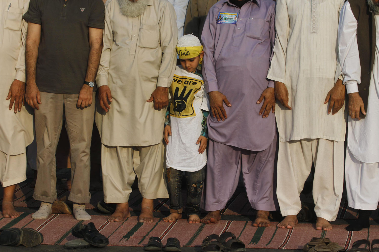 Nov. 24, 2013. A boy stands between supporters of Pakistani religious party Jamaat-e-Islami (JI) and the Pakistan Tehreek-e-Insaf (PTI) political party of former cricket star Imran Khan, as they perform evening prayers during a protest against NATO supply lines in Karachi.