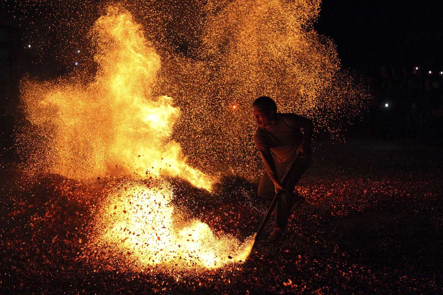Nov. 25, 2013. A man sweeps burning charcoal as he participates in the traditional ritual called  Lianhuo , or  fire walking,  in Pan'an county, Zhejiang province, China.