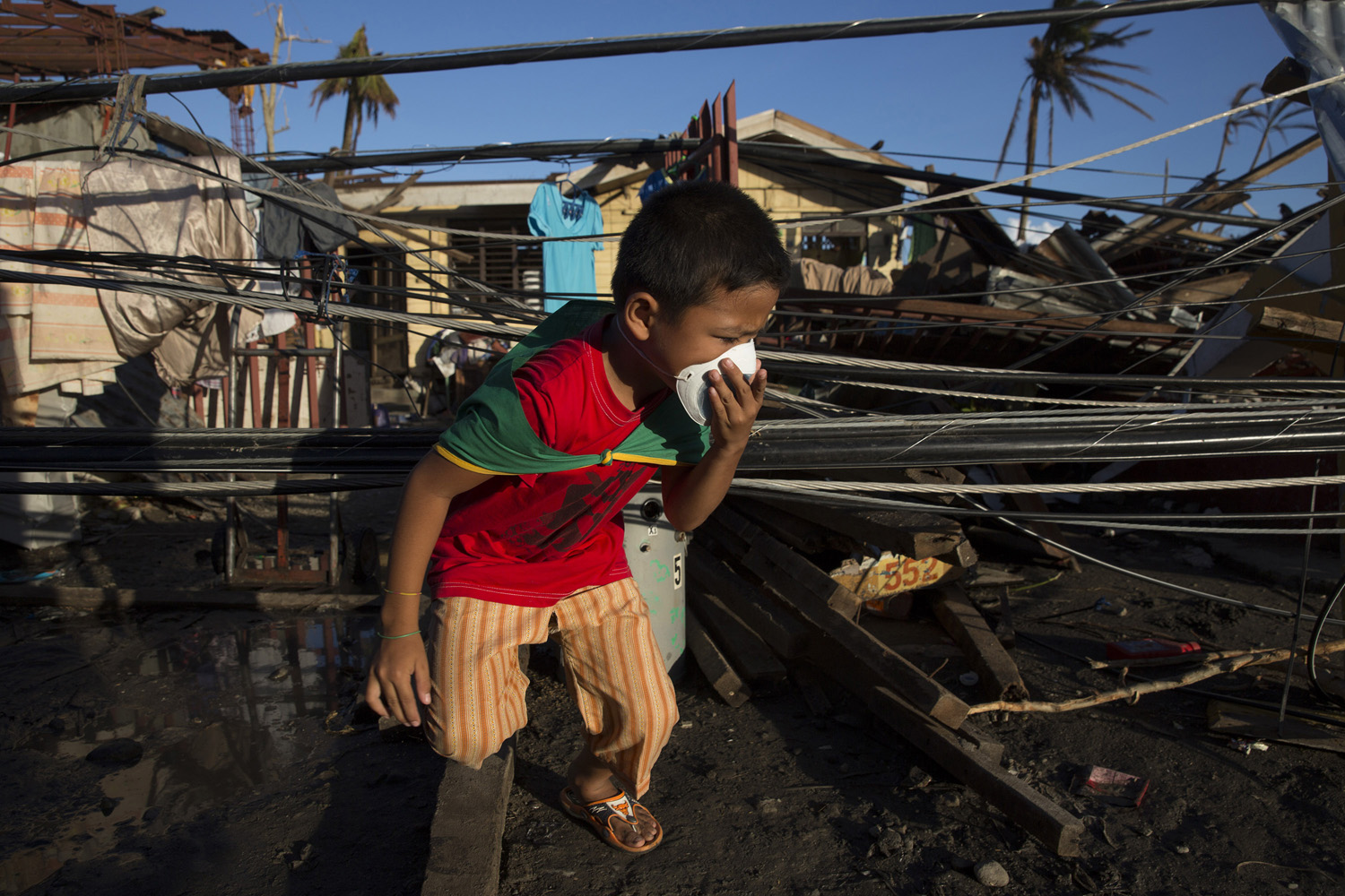 A boy wearing a mask to disguise the smell of dead bodies  clambers through the rubble of homes destroyed by Haiyan Typhoon in Tanuan, The Philippines on November 15, 2013.