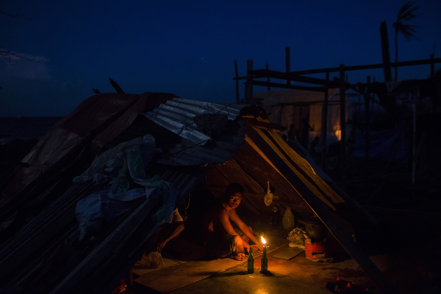 A man who's home was destroyed by Haiyan Typhoon sits by a candle light in the rubble of his home in Tanuan, The Philippines on November 15, 2013.