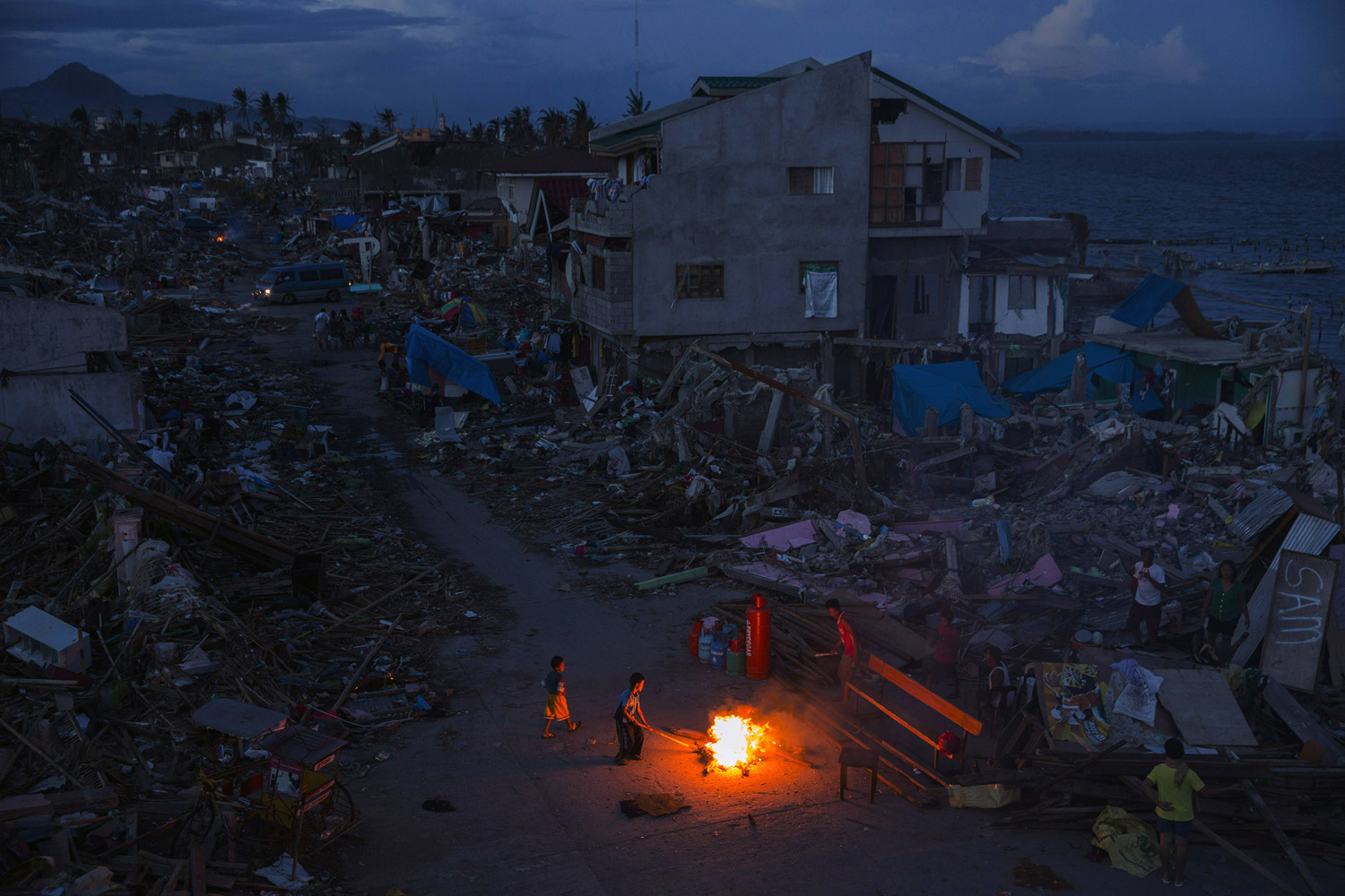 People play by a fire in a neighbourhood destroyed by Haiyan Typhoon in Tacloban, The Philippines on November 16, 2013.