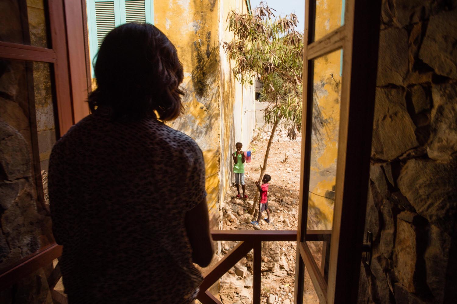 June 27, 2013. First Lady Michelle Obama looks out a window at local children during her visit to a cultural center on Gorée Island, Senegal.
