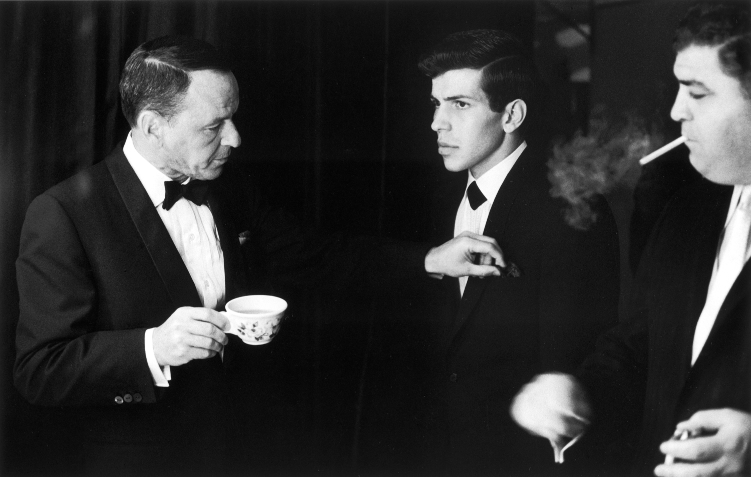 Frank Sinatra adjusts his son Frank Jr.'s pocket handkerchief while bodyguard looks on, Las Vegas, 1965.