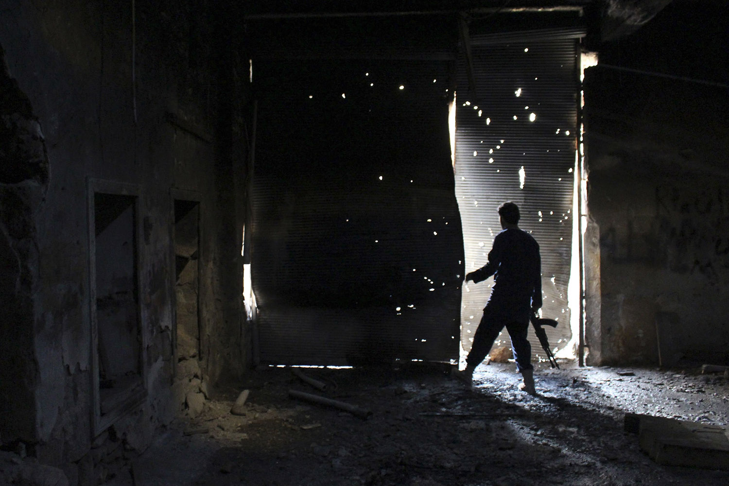 A Free Syrian Army fighter carries his weapon as he peeks out from a damaged shop in Aleppo