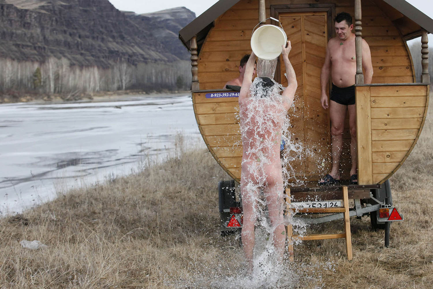A friend of local resident Krasin cools off with cold water after a steam bath in his mobile bathing station on the banks of the Tuba river near the village of Kochergino