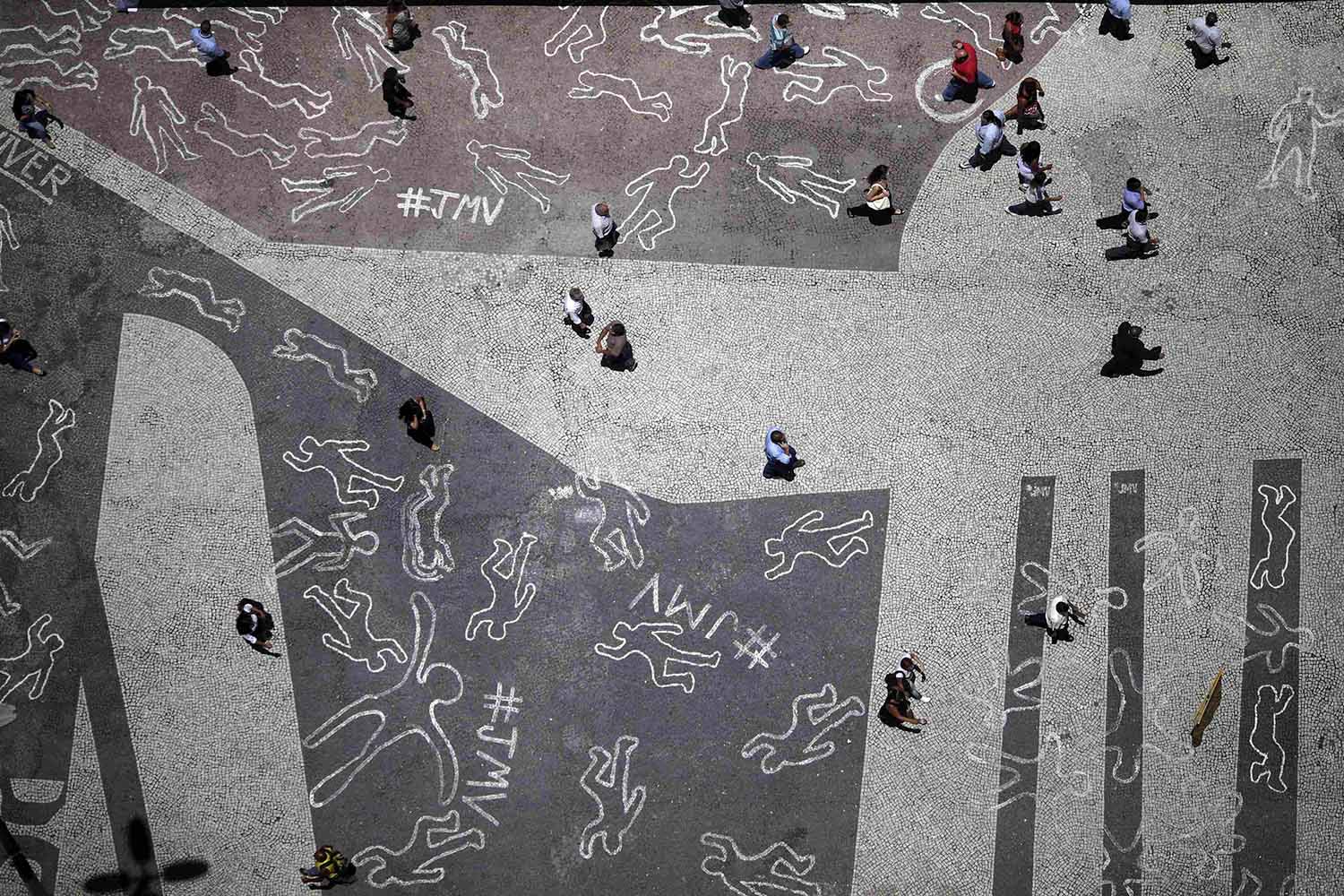 People walk over drawings depicting chalk outlines of bodies during a protest at Carioca square in downtown Rio de Janeiro