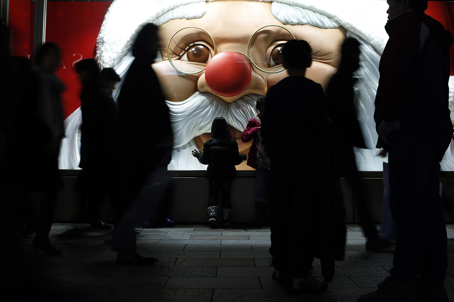 A child looks at a luxury brand store window with a Santa Claus display as people walk past at Ginza shopping district in Tokyo