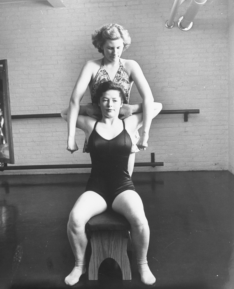University of New Hampshire student Shirley Sylvester (standing) straightens shoulders of sophmore Estelle Dutton in an exercise which aids posture and strengthens pectoral muscles, 1942.
