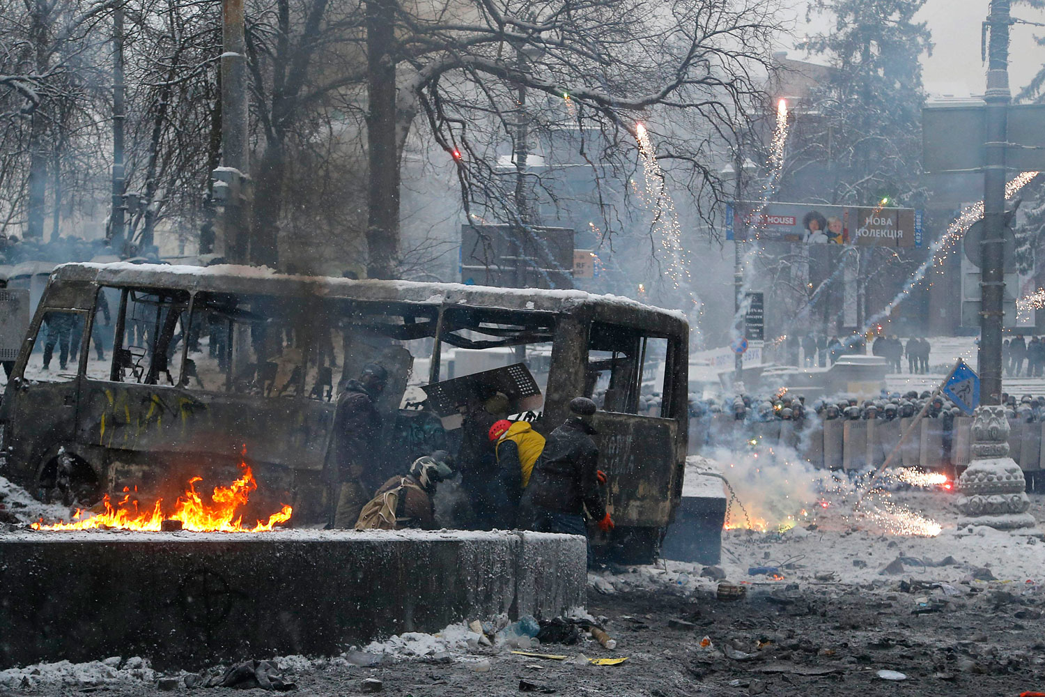Protesters duck behind a burned vehicle as they clash with police in central Kiev, Jan. 22, 2014.