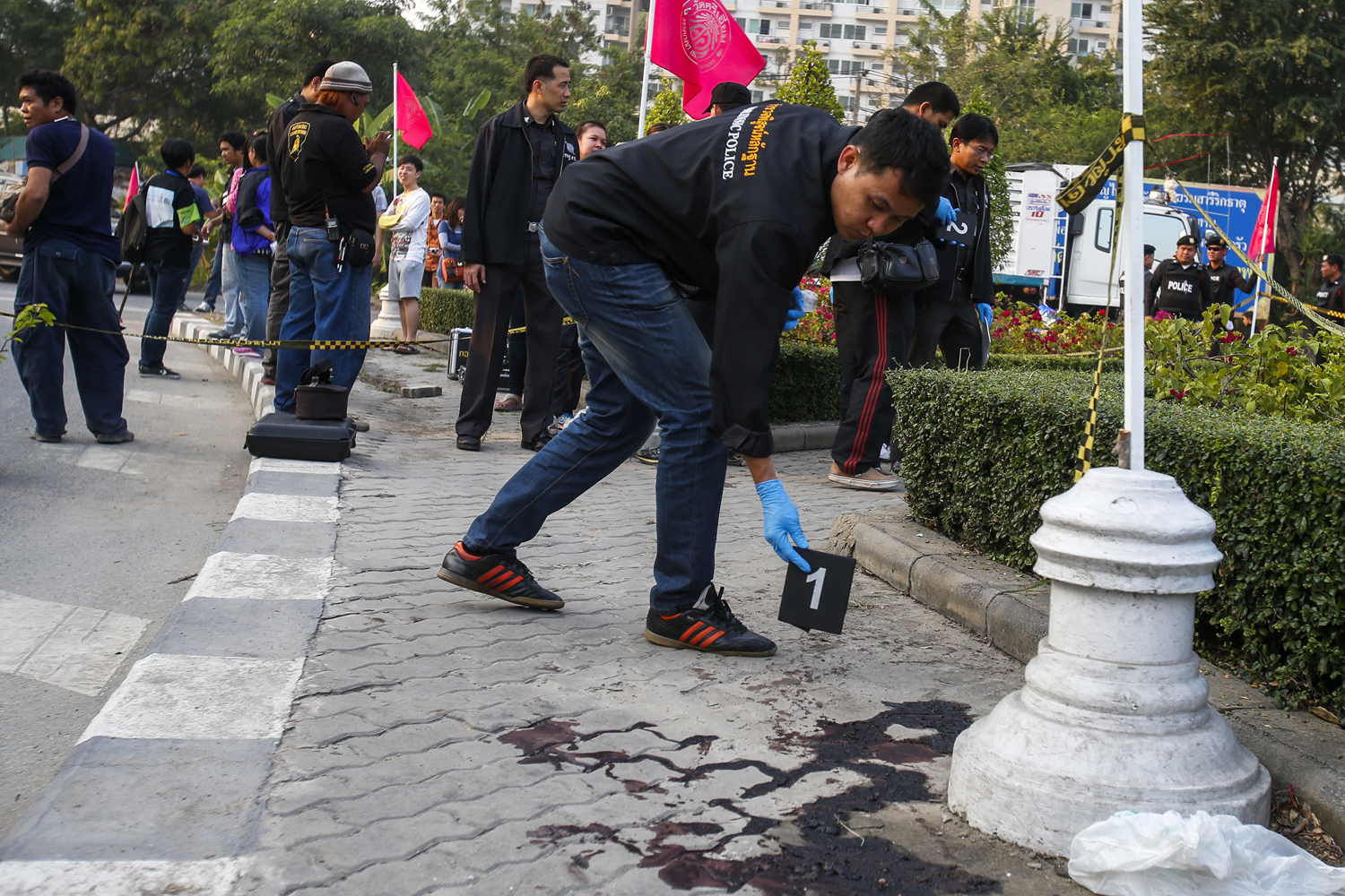 A forensic police officer drops a marker next to blood at the site of what police say was clashes between anti-government protesters and supporters of PM Yingluck Shinawatra in Bangkok