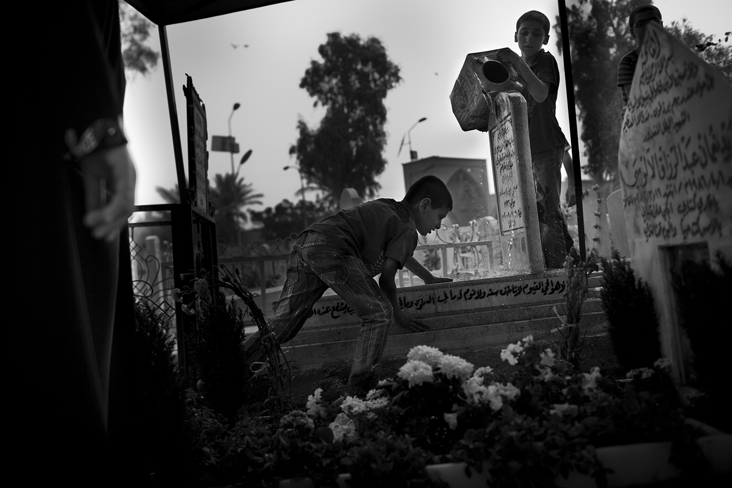 Apr. 18, 2012. Baghdad. Three children clean a grave with water from a battered canister at a cemetery.