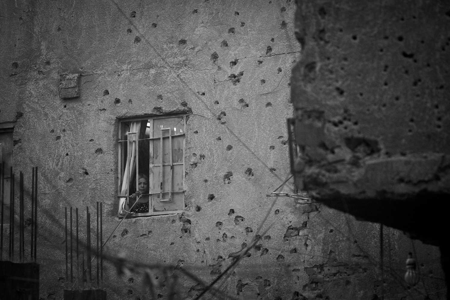 Apr. 19, 2012.  Hurriya District, Baghdad. A woman looks out the window of her house riddled with bullet holes.