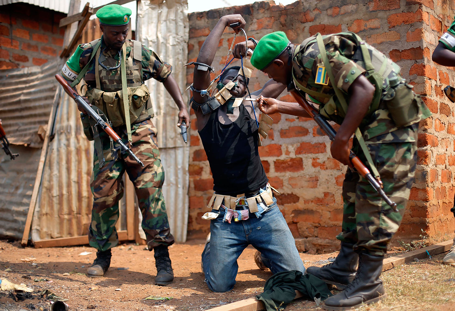 Rwandan African Union peacekeepers remove the lucky charms from a suspected Anti-Balaka Christian man who was found with a rifle and a grenade following looting in the Muslim market of the PK13 district of Bangui, Jan. 22, 2014.