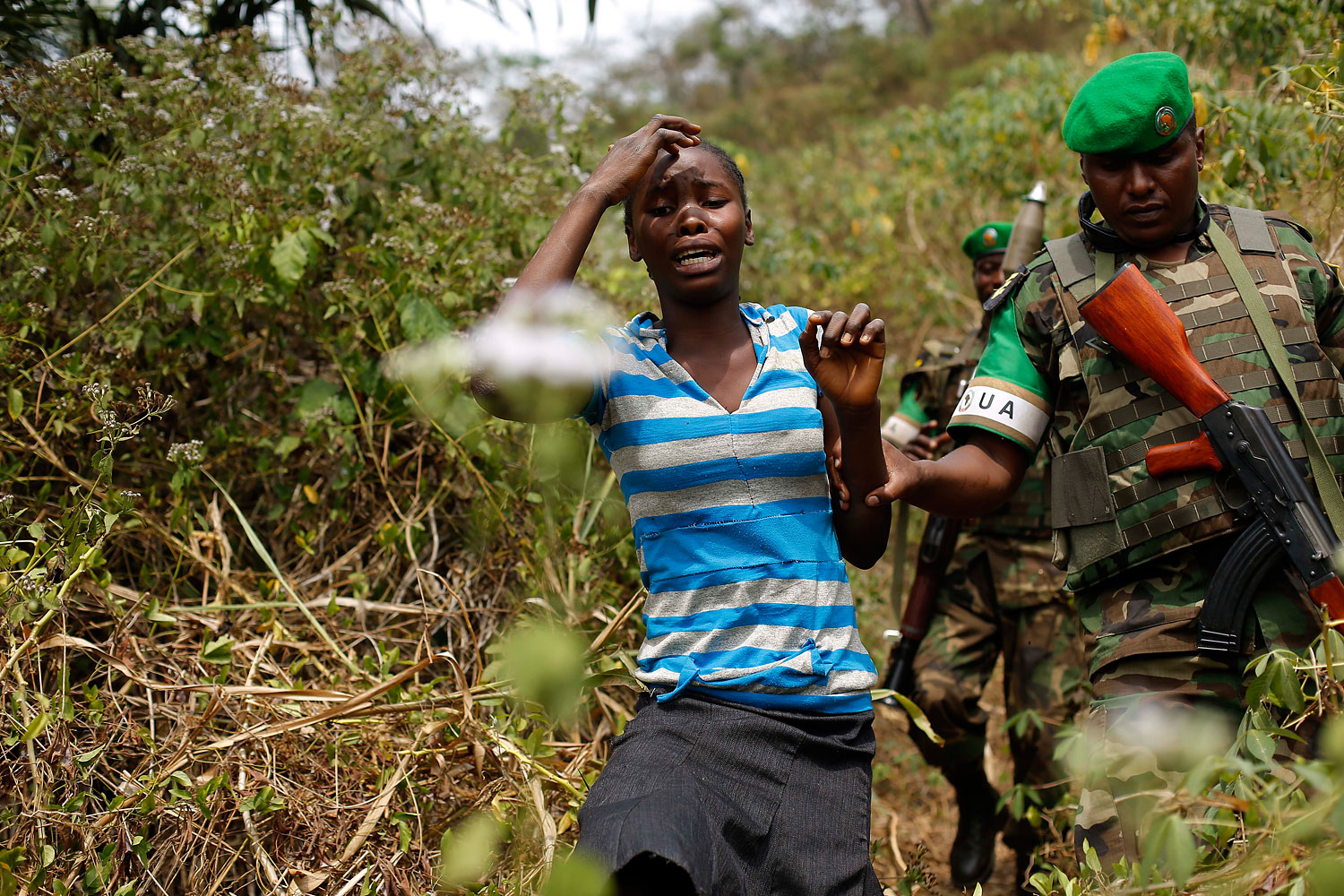 A terrified woman walks down from the bush in the hills 10 miles outside Bangui, Jan. 24, 2014, as Rwandan troops tell her to calm down during a weapons search operation.
