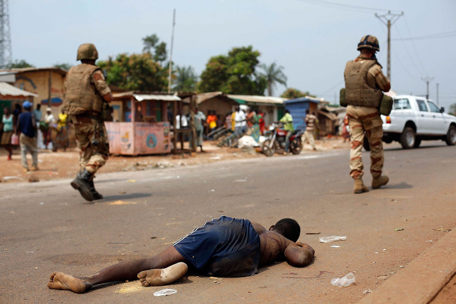 The body of a man who was killed by a mob that believed him to be a Seleka Muslim militia member lies on the ground near the PK11 checkpoint as French soldiers walk by in Bangui, Jan. 24, 2014.