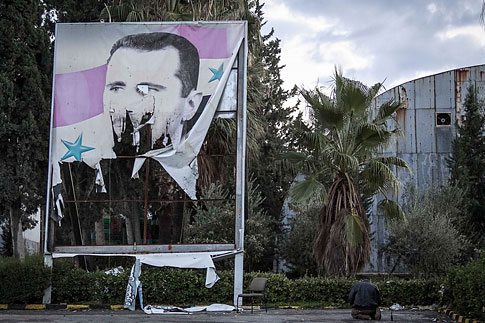 A Free Syrian Army fighter offers evening prayers beside a damaged poster of Syria’s President Bashar Assad during heavy clashes with government forces in Aleppo, Syria, on Dec. 8, 2012. (Narciso Contreras / AP)