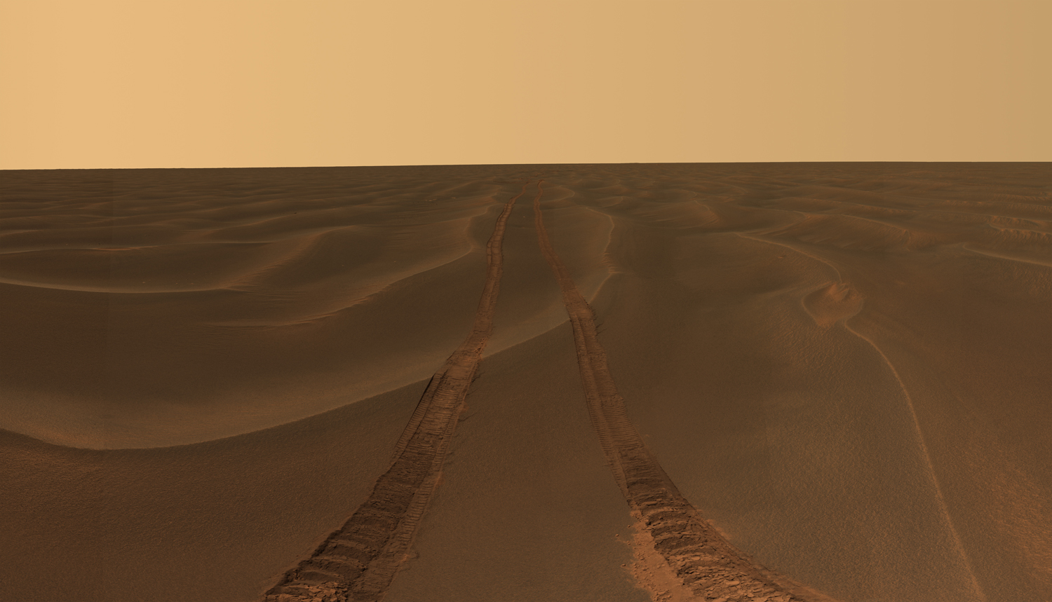 Rover tracks disappear toward the horizon like the wake of a ship across the desolate sea of sand between the craters Endurance and Victoria on the Meridiani Plains.