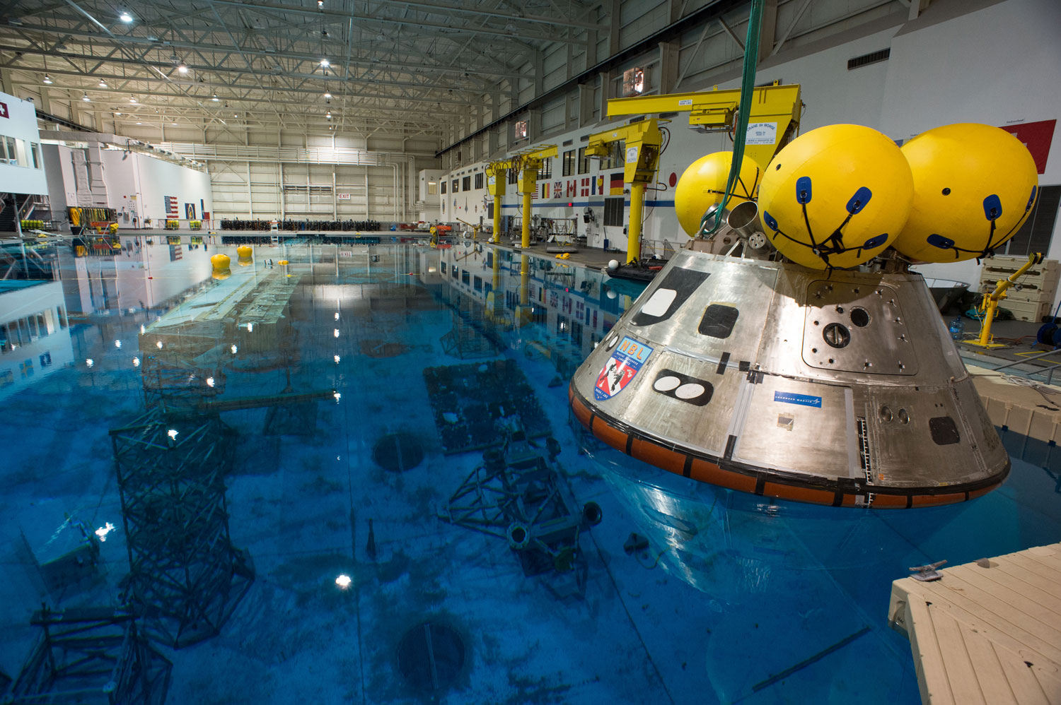 A model of Orion floats above an underwater mockup of the International Space Station in the 40-foot (12 m) deep Neutral Buoyancy Laboratory in Houston on April 25, 2013. The model is used to practice splashdown operations for Orion's first flight test in 2014. The yellow balls on the top of the capsule are flotation balloons which would flip the vehicle into the proper orientation if it were to turn upside down after landing.