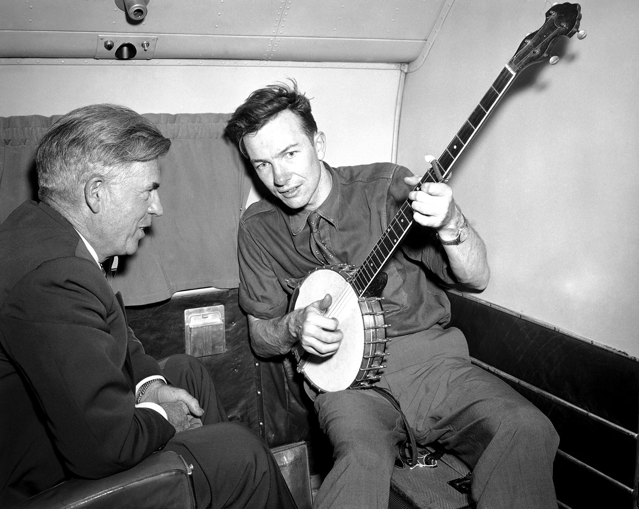 From left: Henry A. Wallace, making a political tour of the American South, listens to Pete Seeger play the banjo on a plane between Norfolk and Richmond, Aug. 28, 1948.