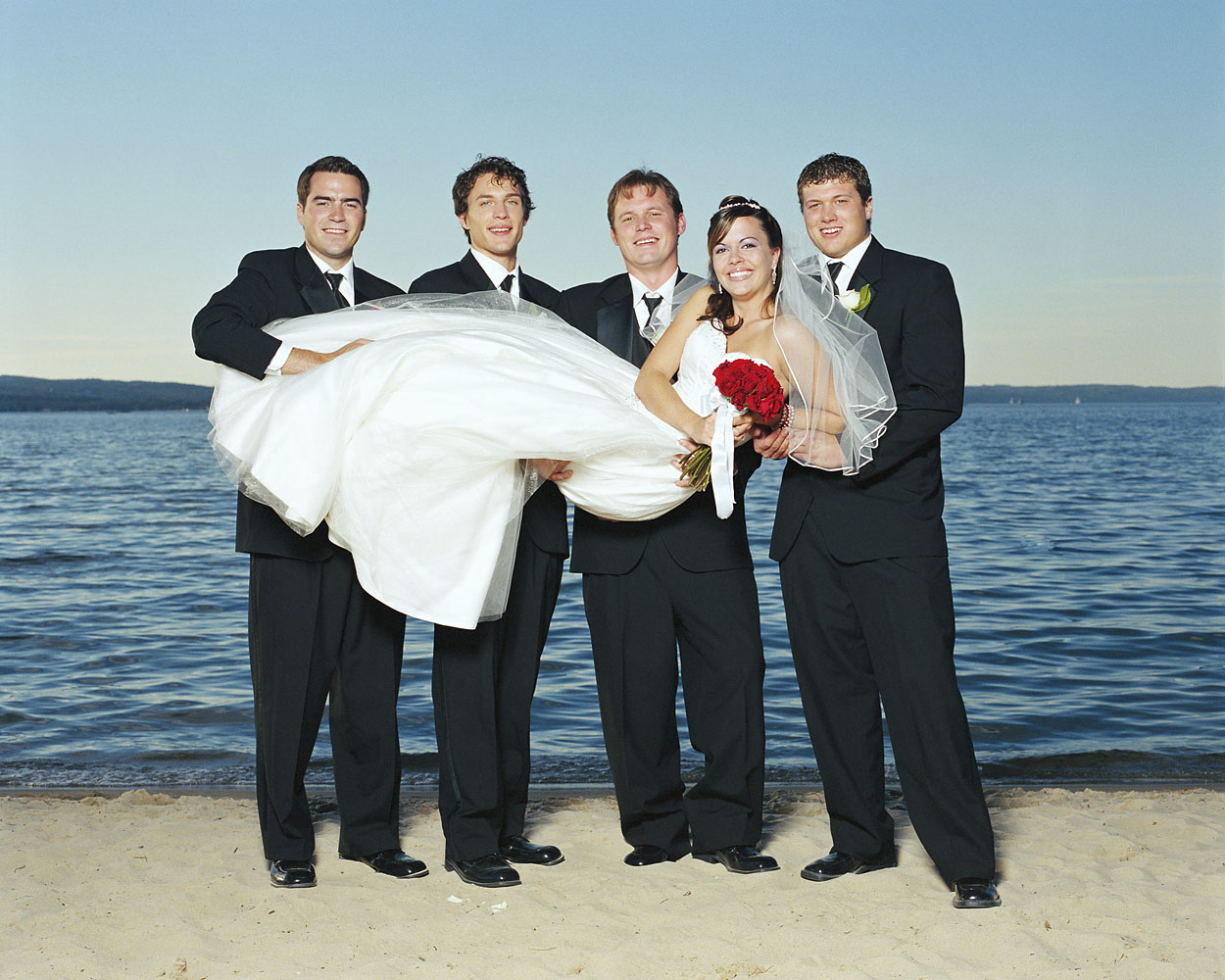 Groom and groomsmen holding bride on beach smiling, portrait